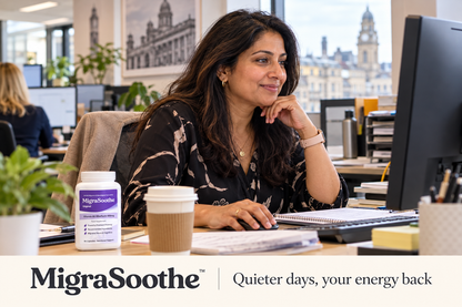An Indian British woman working at her computer in a Leeds office, with coffee and a MigraSoothe Original bottle on her desk.
